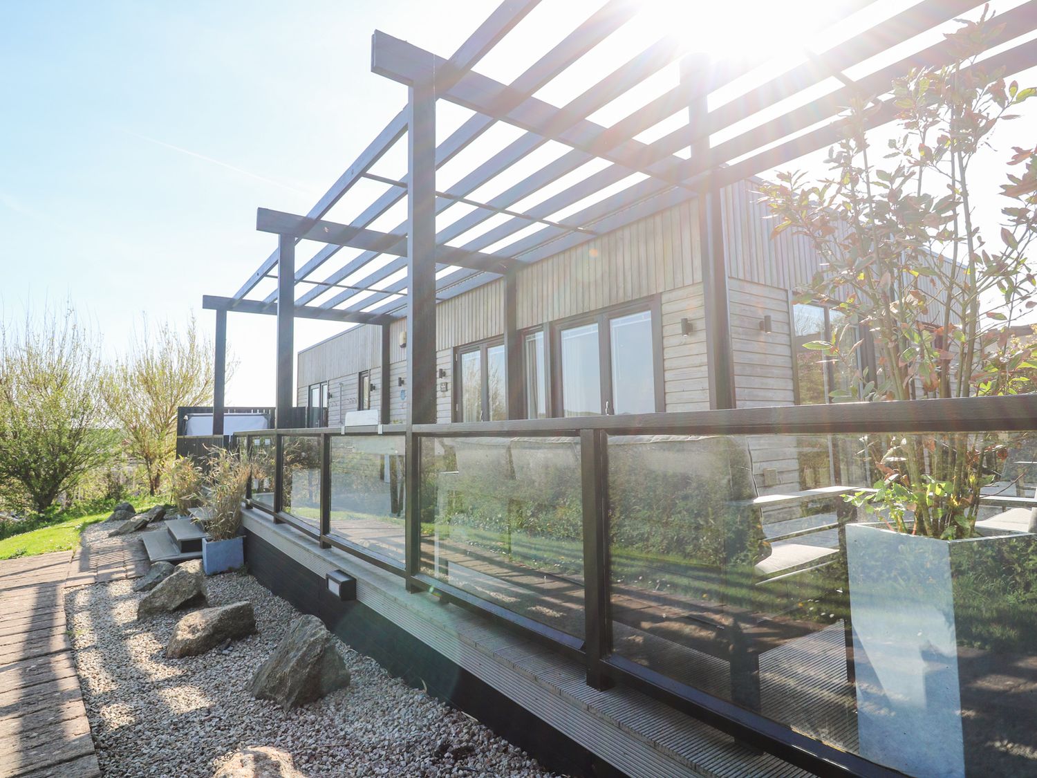 A wooden exterior patio with glass railing and plants at Bay View in Portreath