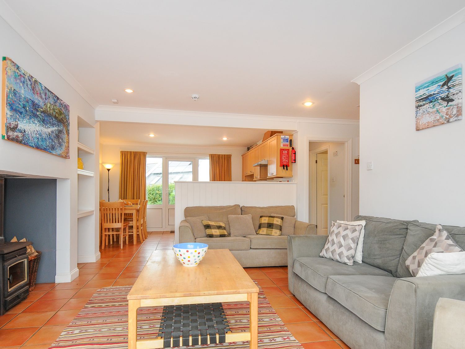 An open living room with two sofas a wooden coffee table a dining table and chairs with a kitchen in the background at Bryher in Trebetherick near Polzeath