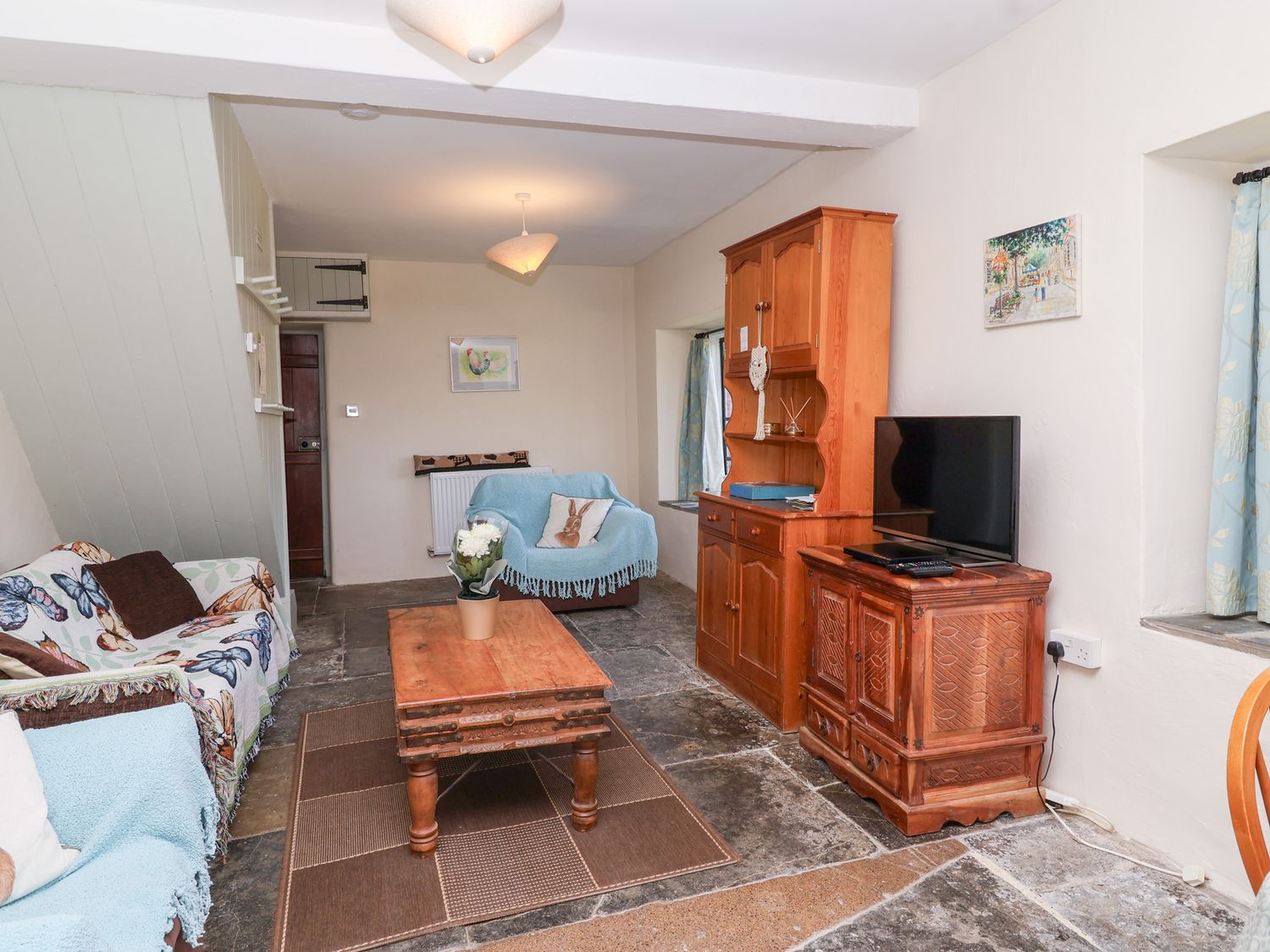 A living room with two armchairs covered in throws a wooden coffee table a wooden cabinet and a television at Hyde cottage Sutton Bingham near Yeovil Somerset