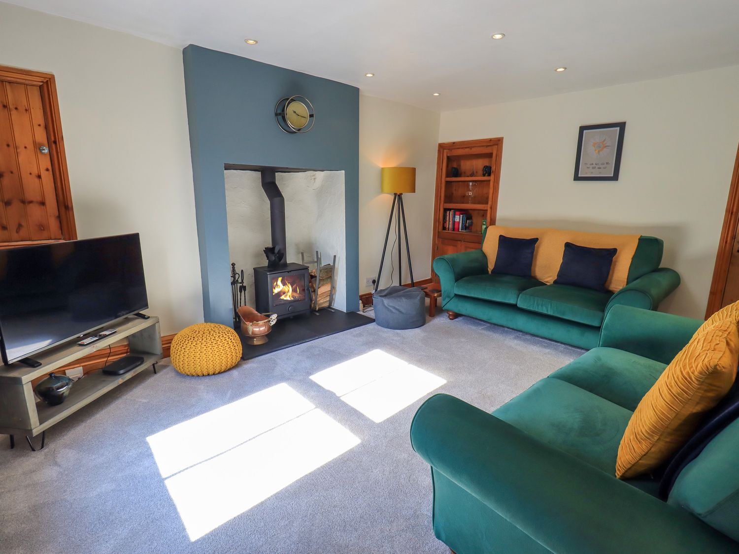 A living room with green sofas a wood burning stove a television and a floor lamp at Fettlers Cottage 51 High Street Kirkby Stephen
