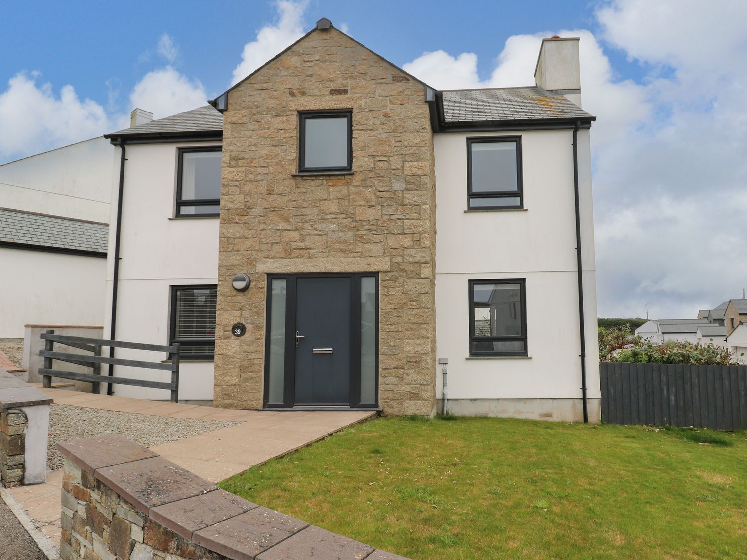 A modern two-story house with stone and white exterior walls and a lawn at 39 The Shrubberies in Porthleven