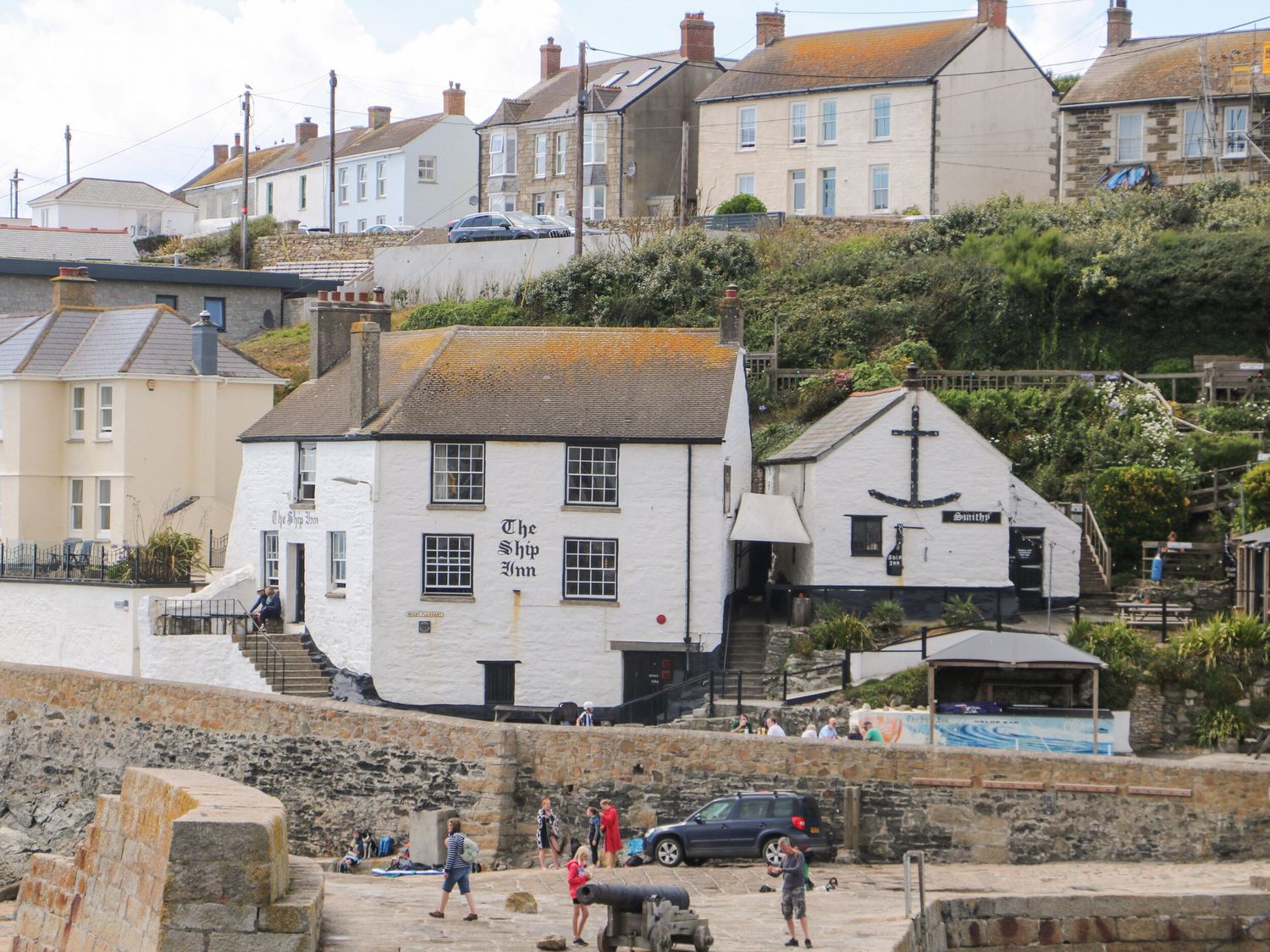 A white building named The Ship Inn near a stone harbor with people walking at 39 The Shrubberies in Porthleven