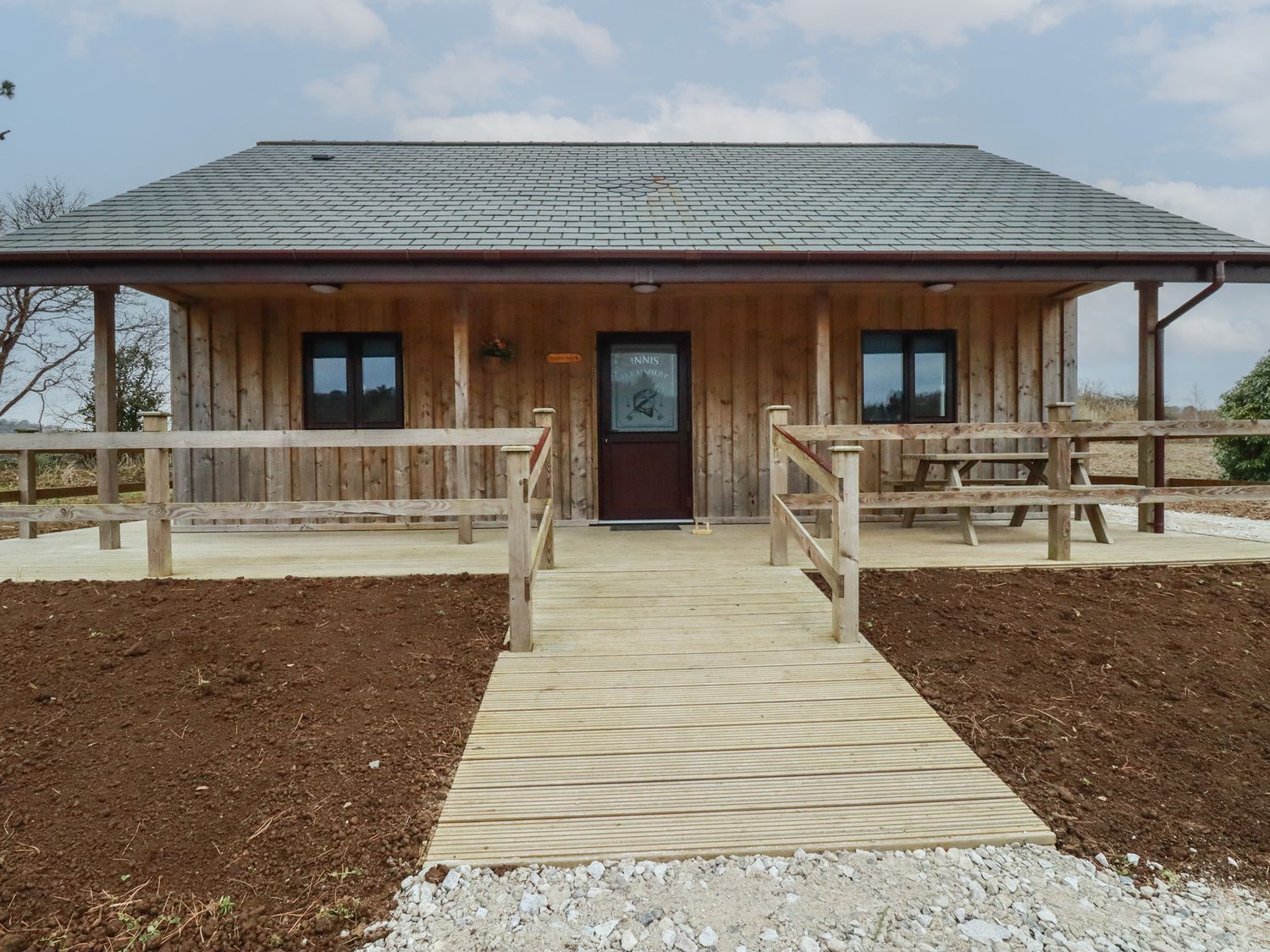 A wooden cabin with a ramp and a picnic table on the porch at Kingfisher Lodge in Treverbyn near St Austell