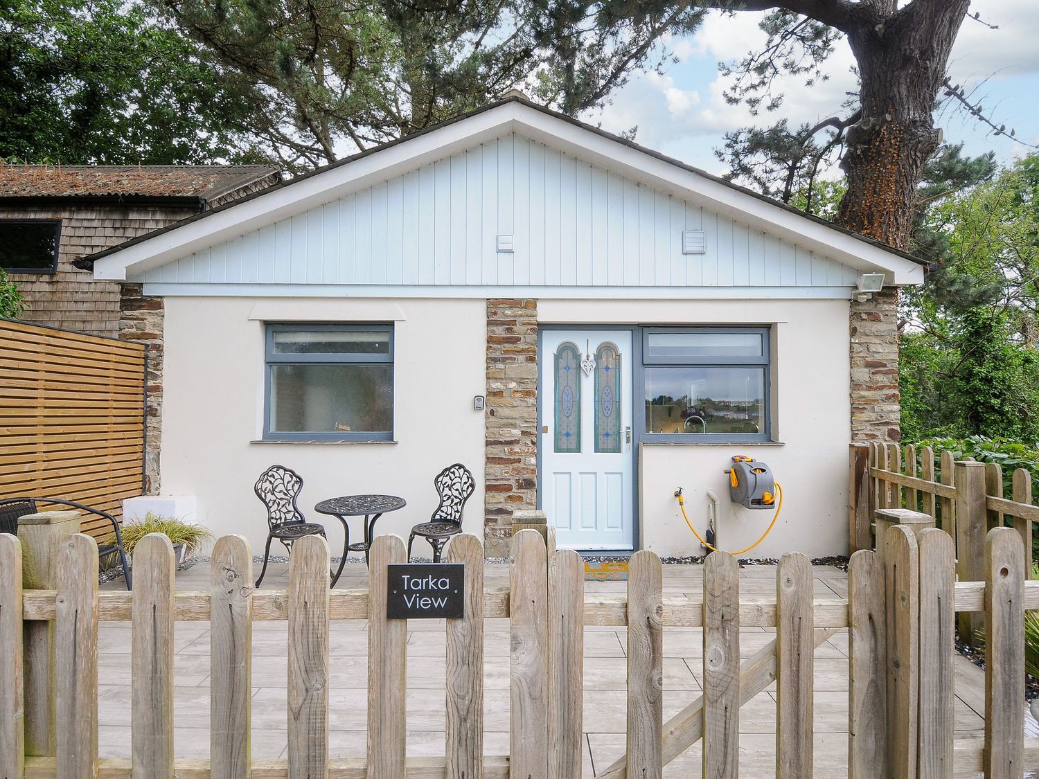 A small white house with two windows a door and a wooden fence in front at Tarka View in Bideford