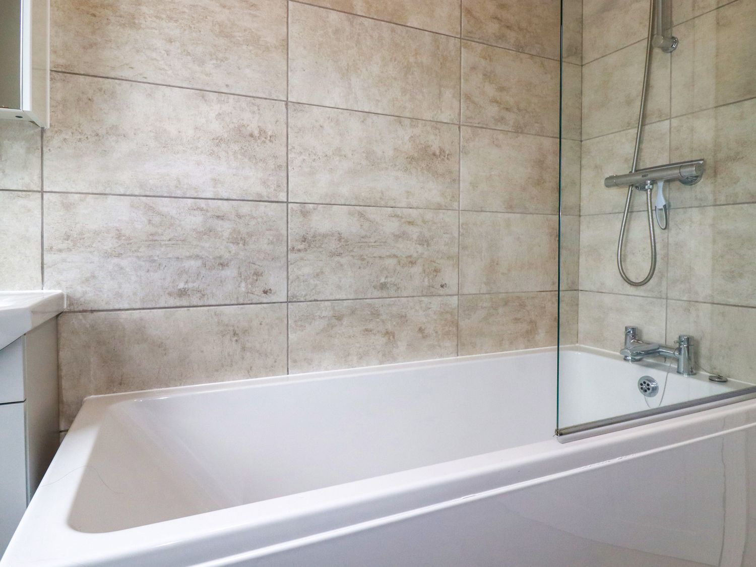 A bathtub with a shower head and tiled walls in a bathroom at 14 Beech Road in St Austell