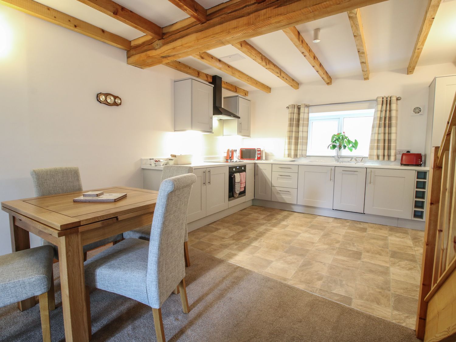 A kitchen with wooden dining table and four upholstered chairs wooden ceiling beams and light gray cabinets at Ascot in Knolton near Ellesmere