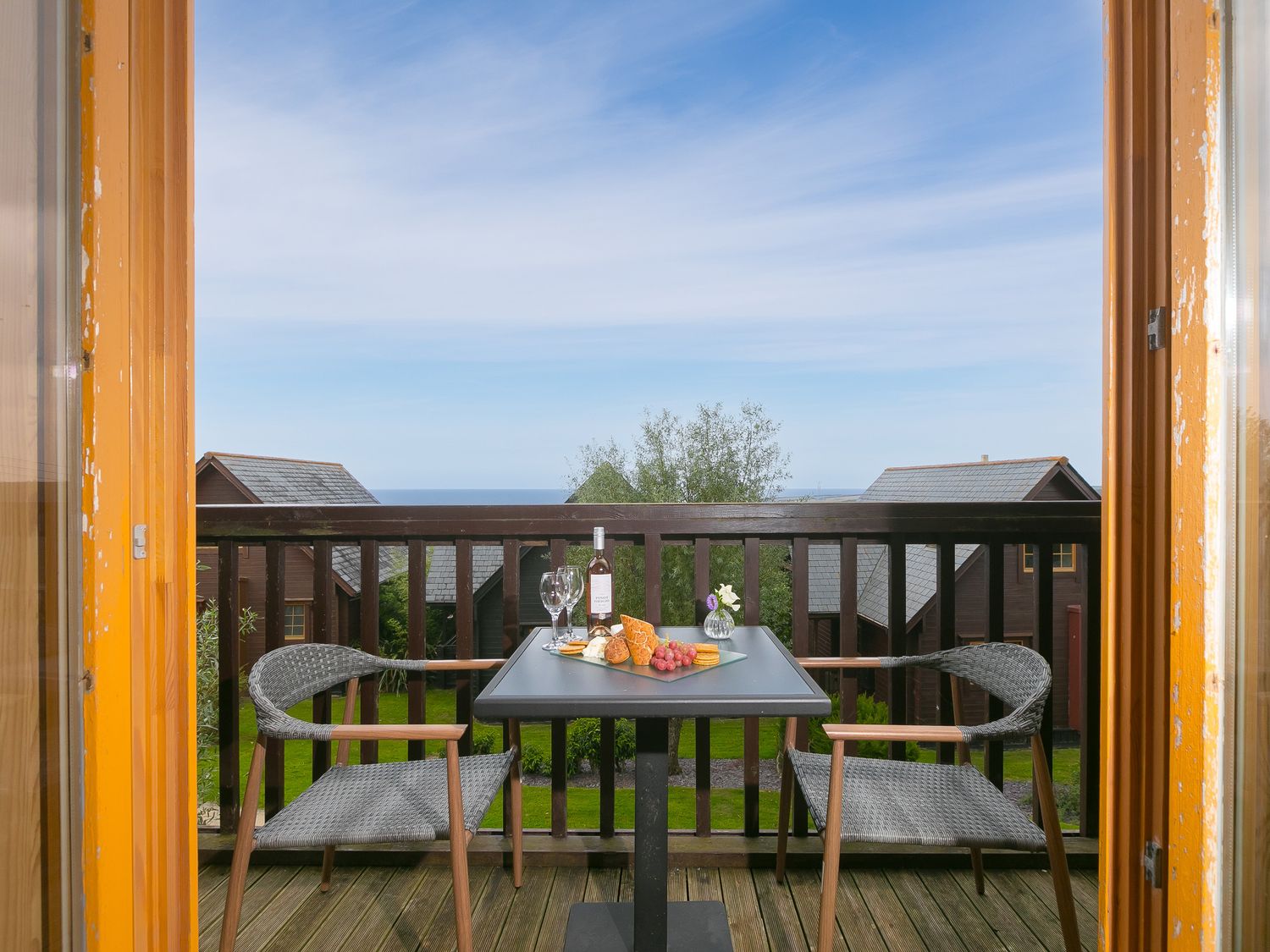A balcony with two chairs and a table set with wine and snacks overlooking houses and the sea at Trevaunance in Portreath