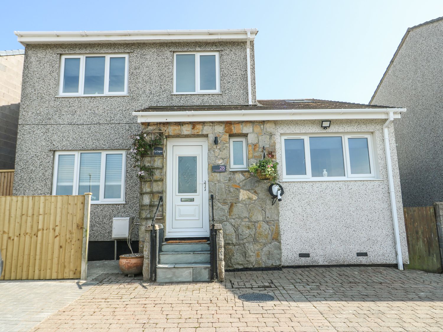 The front view of a two-story house with multiple windows a white door stone and pebble dash exterior and a driveway at Ty Copr in Amlwch