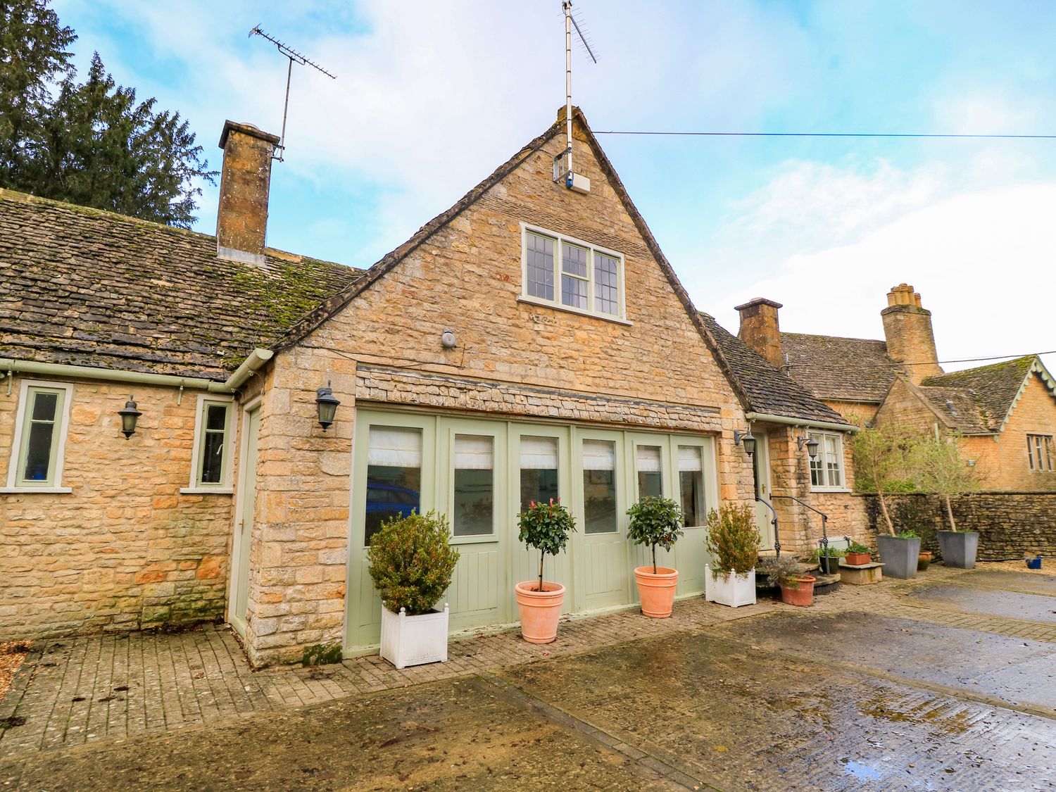 A stone house with green doors and potted plants outside at The Elm Coach House in Chipping Norton