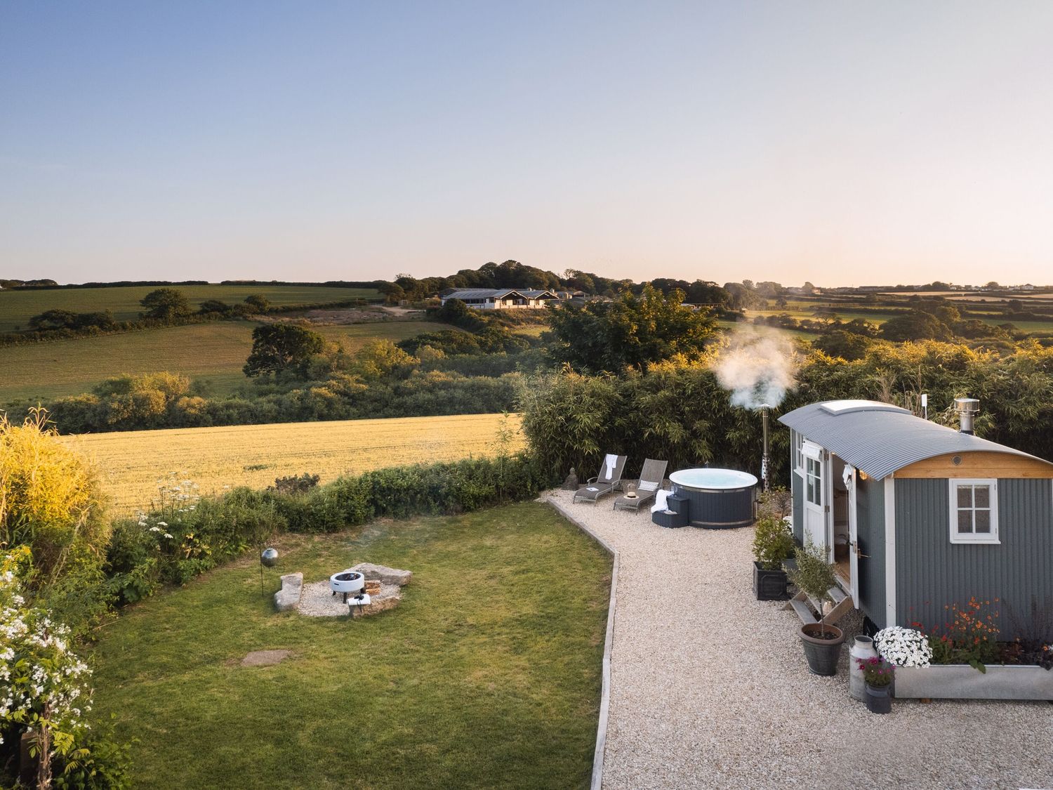 A garden with a fire pit a hot tub loungers and a small cabin near fields at Stargazer in St Erme near Truro