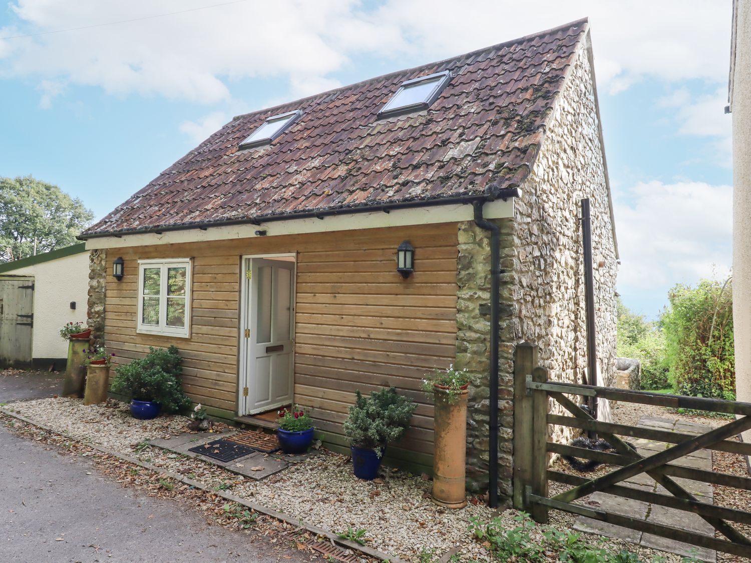 A small house with stone and wood exterior a tiled roof and potted plants outside at The Wheelhouse Beacon near Yarcombe