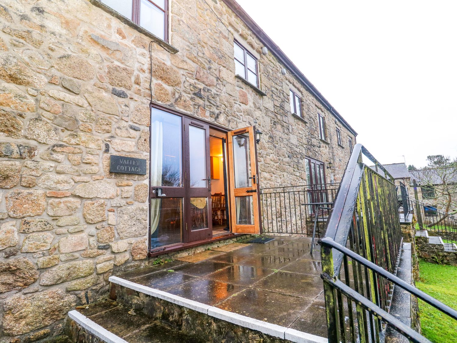 Stone exterior of a building with a door opening to a patio with a metal railing at Valley Cottage in Penzance
