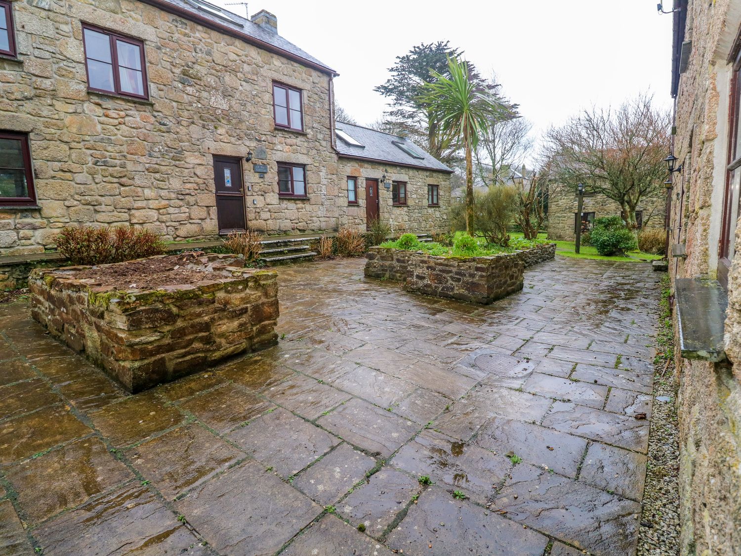 Stone paved courtyard with two raised stone planters and surrounding stone buildings at Valley Cottage in Penzance