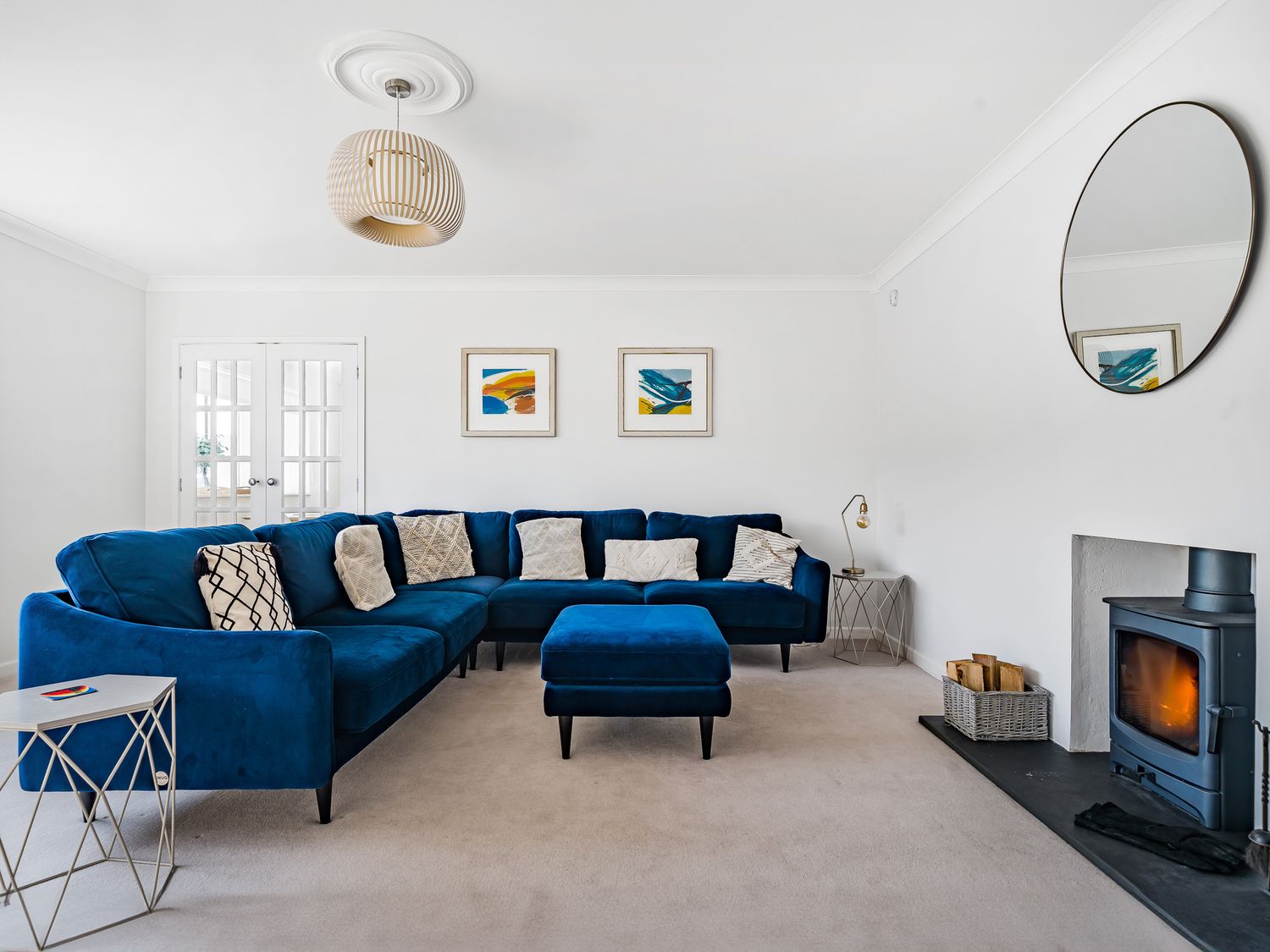 A living room with a blue sectional sofa a blue ottoman a wood burning stove and circular mirror at Fairwinds in Portreath