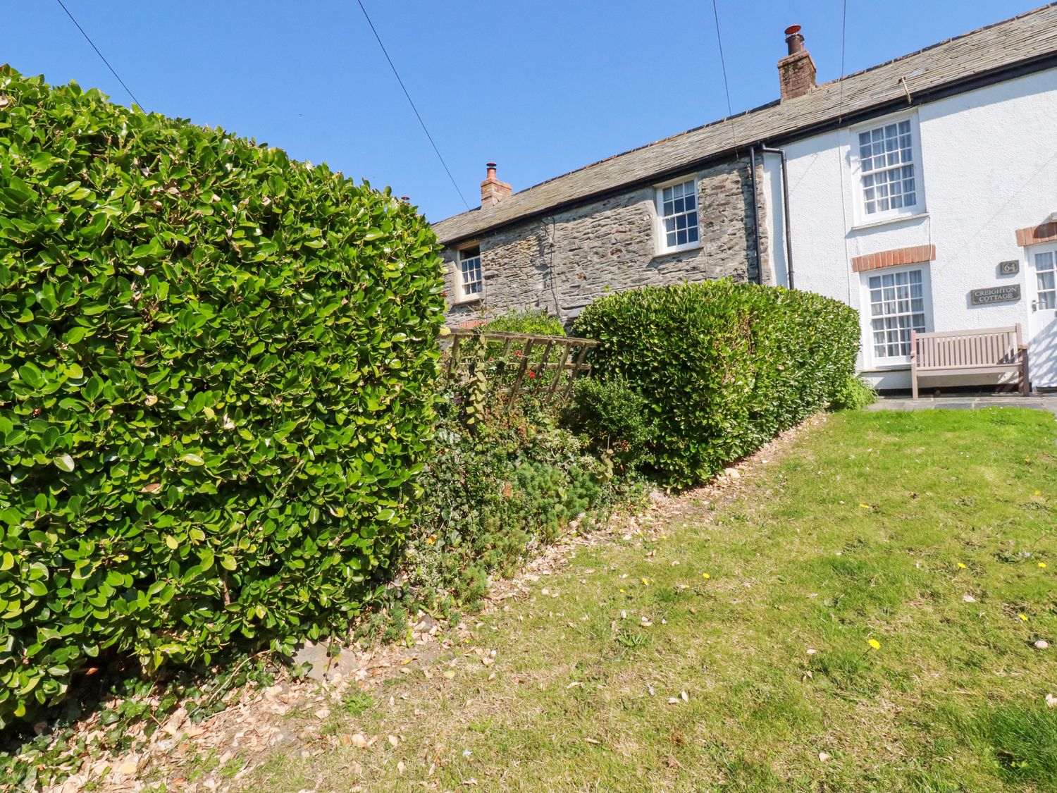 A cottage with stone and white walls surrounded by green hedges and a lawn at Creighton Cottage in Port Isaac