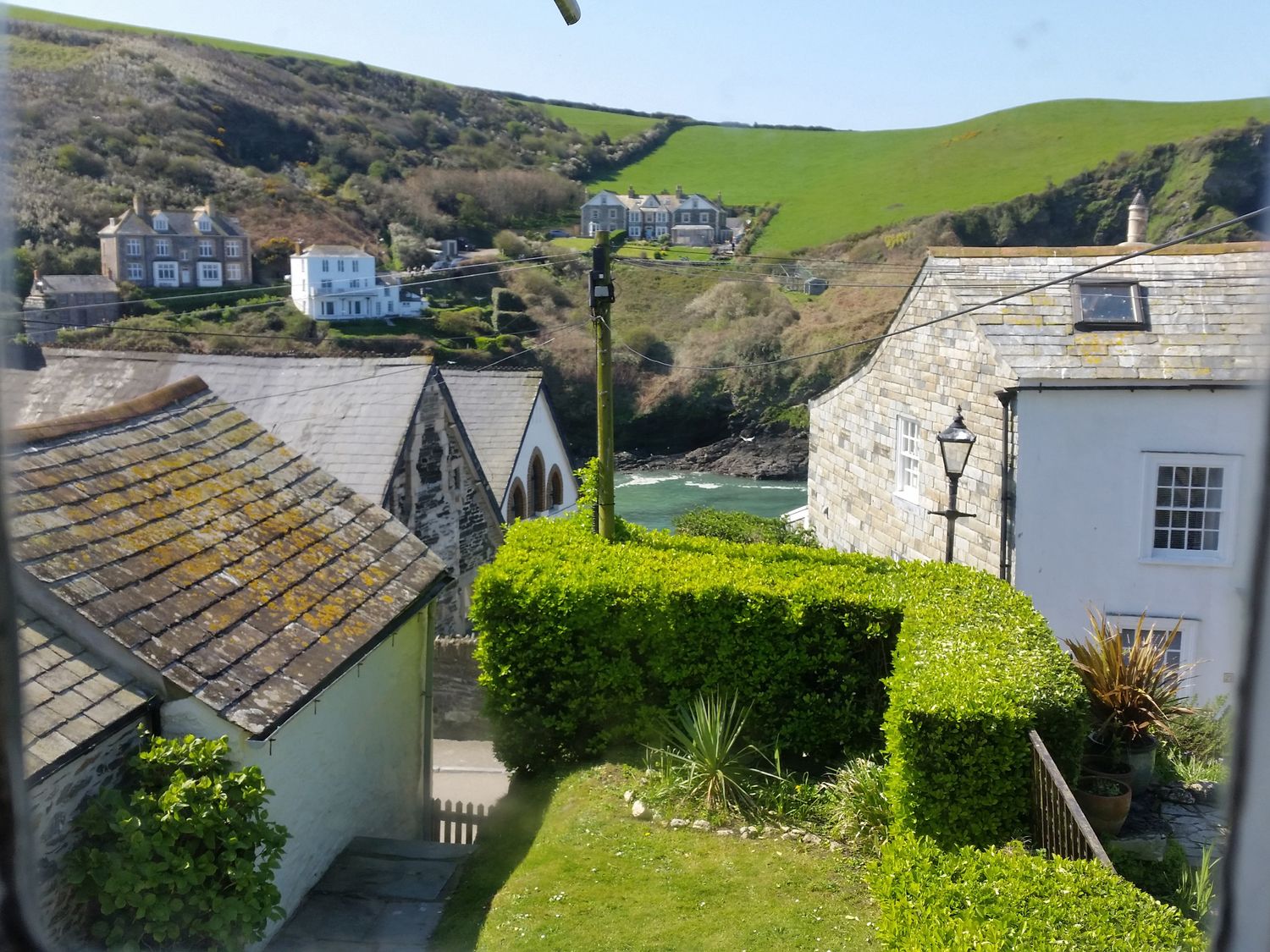 A coastal village with stone houses green hedges and hills with water in the background at Creighton Cottage in Port Isaac