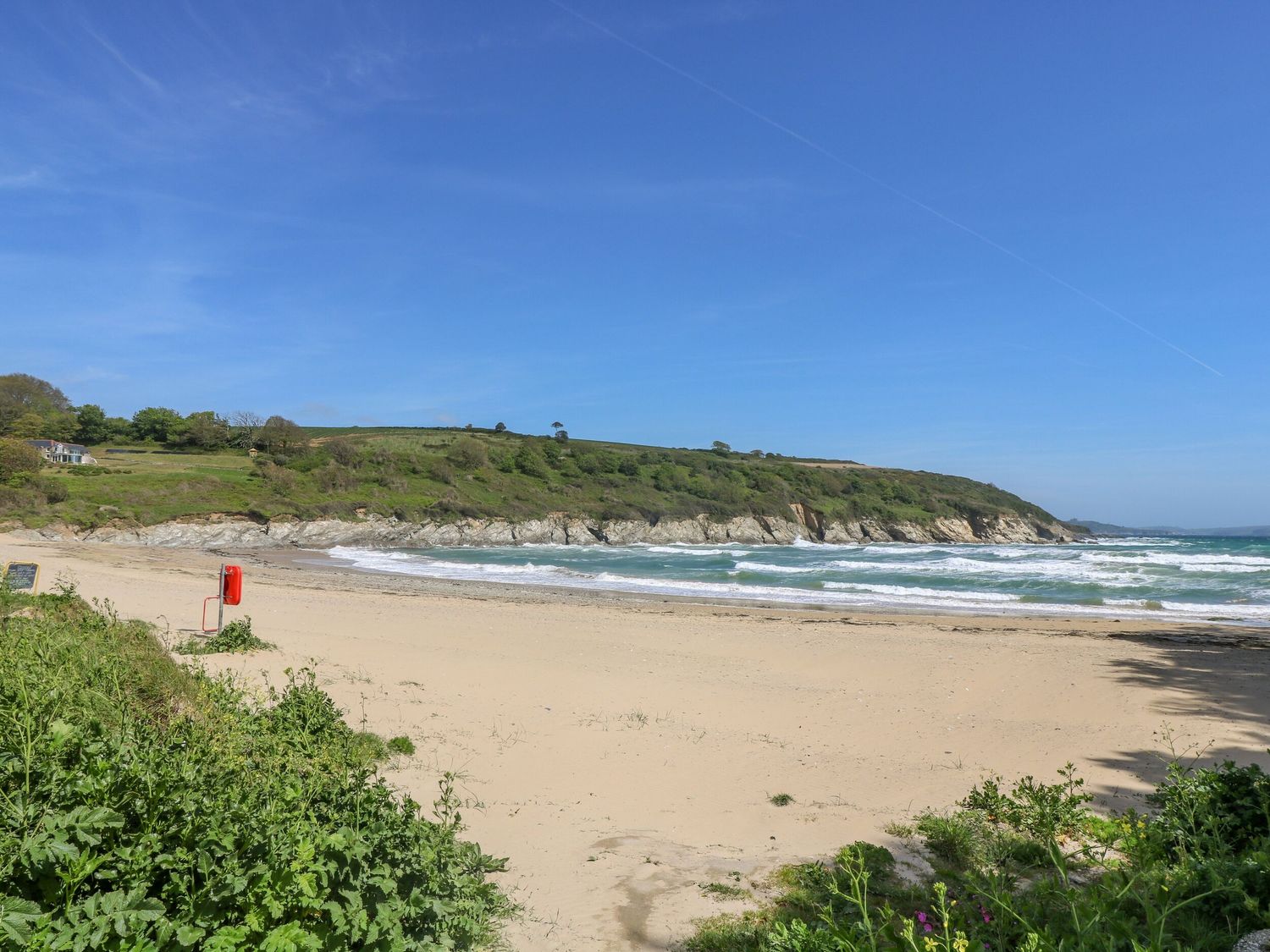 A sandy beach with waves and green hills in the background at Chy Lowena Goldenbank near Budock Water