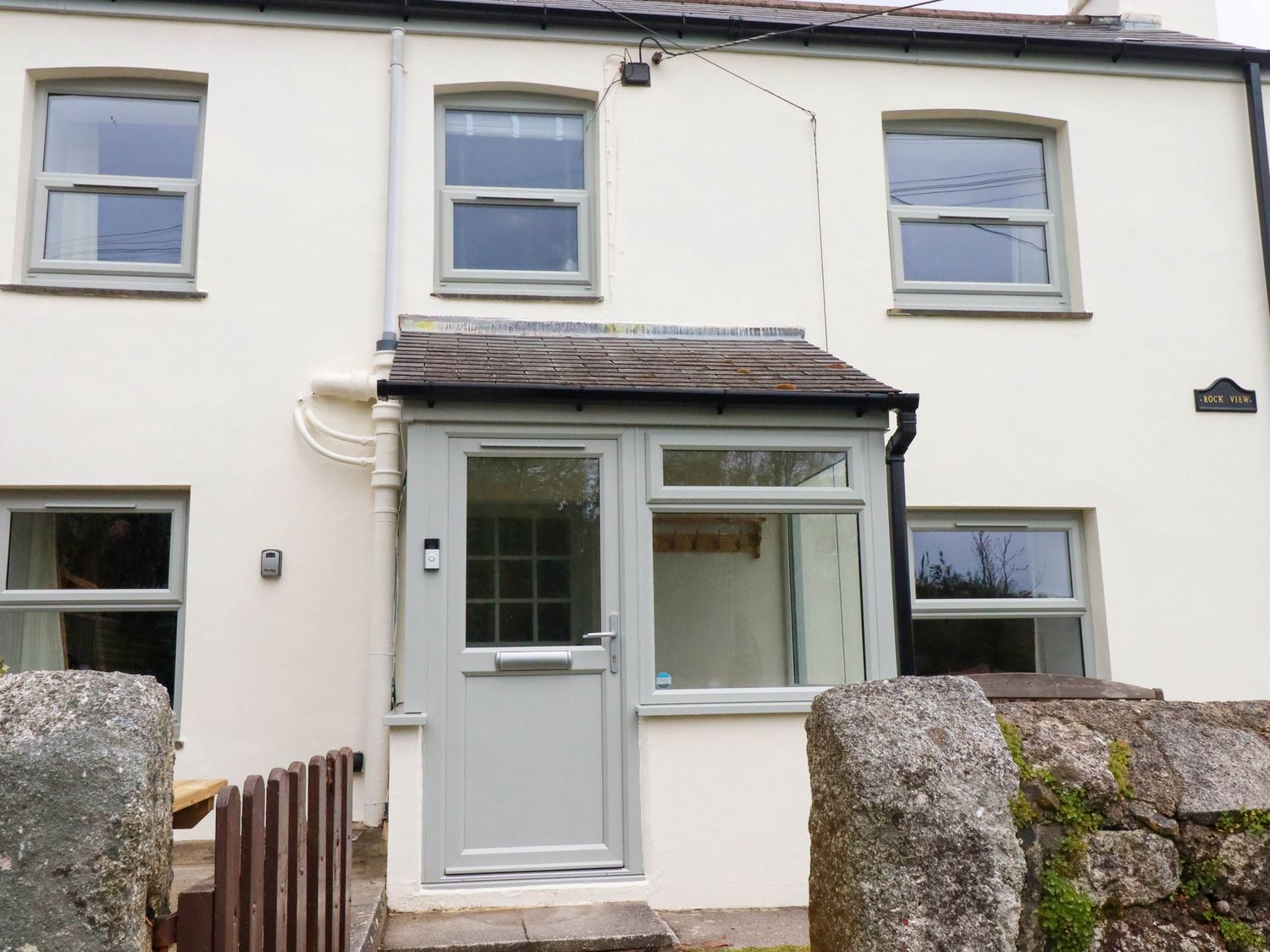 Front view of a two-story house with a small porch and stone wall at Rock View in Trethurgy near St Austell
