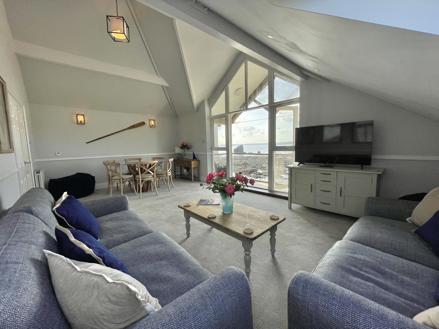 A living room with two sofas a coffee table a dining table and large windows with a sea view at 12 Thurlestone Rock in Thurlestone