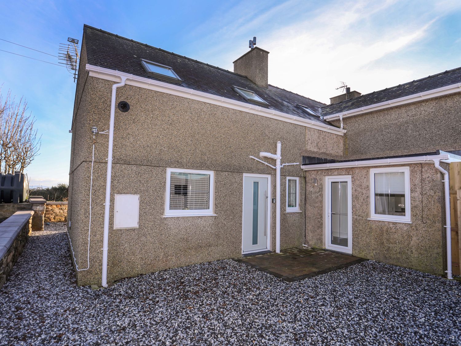 The exterior of a two-story house with a gravel yard and skylights on the roof at Ty'n Ffridd Bach in Chwilog near Y Ffor
