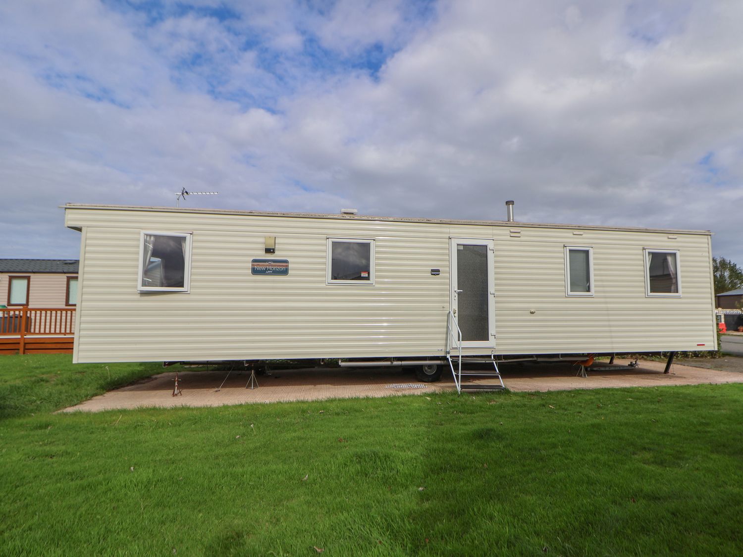 A beige mobile home with four windows and a door with steps on a grassy plot at Herrylock in Rhyl