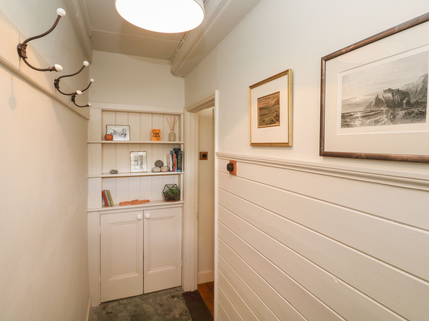 A hallway with a built-in shelving unit a row of coat hooks and framed pictures on the wall at Apple Tree Cottage in Gweek
