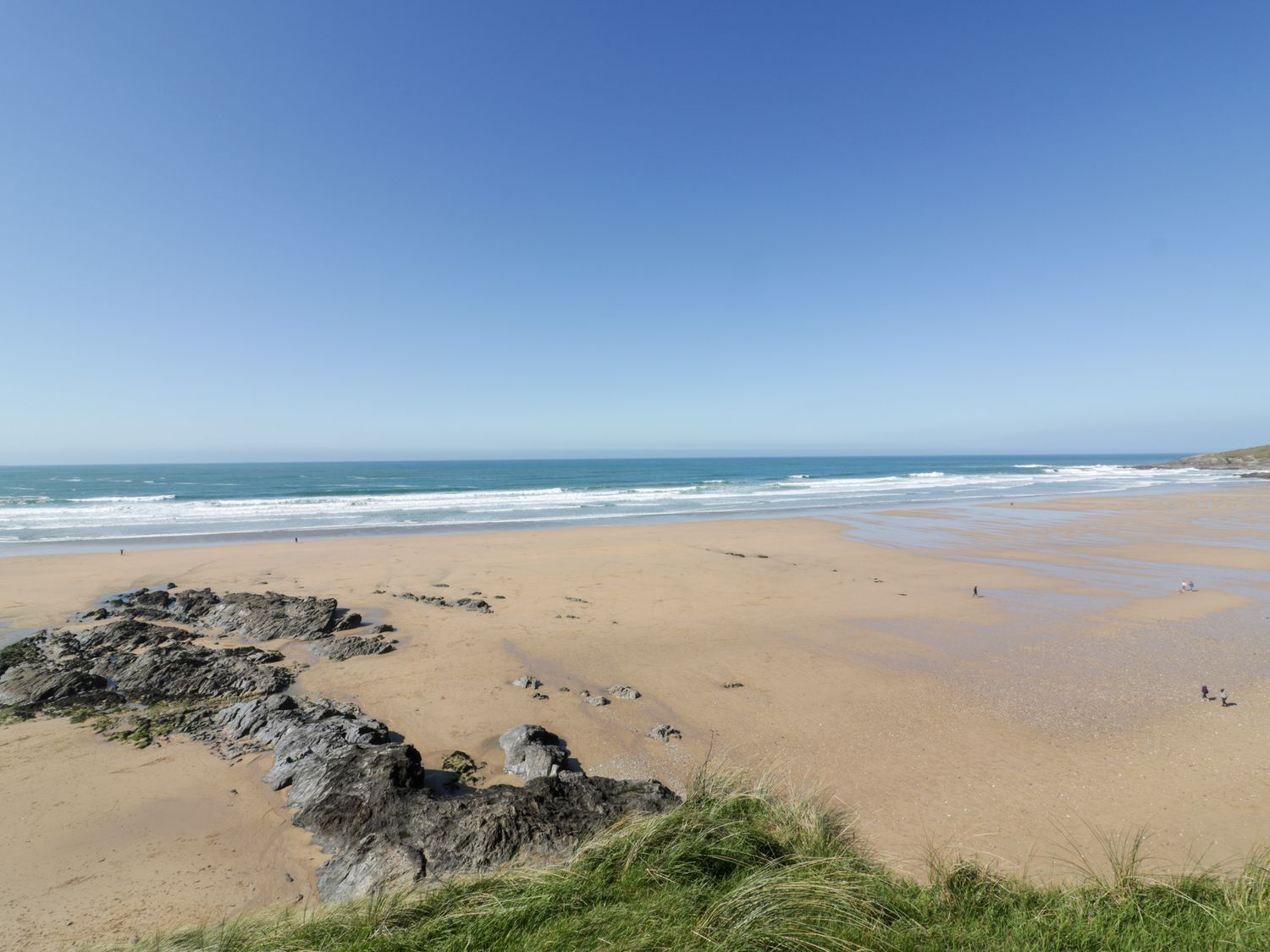 A sandy beach with rocks and waves under a clear sky at Fistral Tide in Newquay