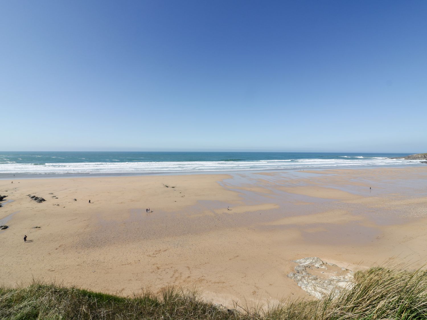 A wide sandy beach with a few people walking near the ocean at Fistral Tide in Newquay