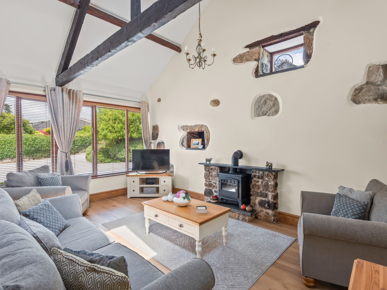 A living room with sofas coffee table wood burning stove and large window at The Dairy in St Neot