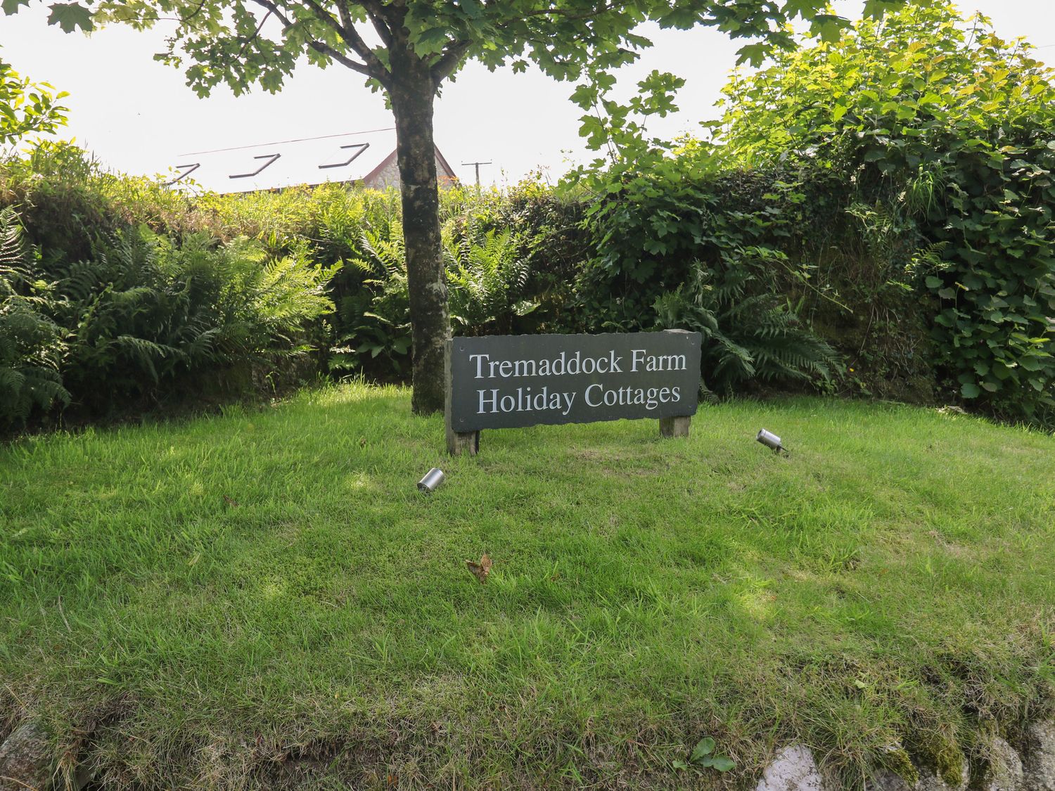 A sign for Tremaddock Farm Holiday Cottages on grass with trees and bushes behind at The Dairy in St Neot
