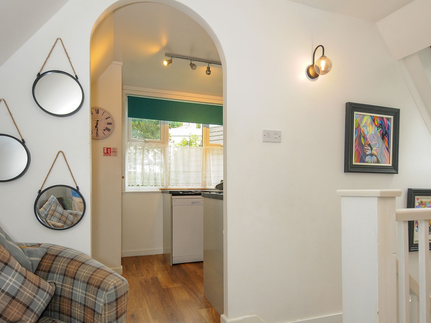 An archway leading to a kitchen with a window and dishwasher a plaid armchair and three round mirrors on the wall at Valley Lodge 20 in St Ann's Chapel near Callington