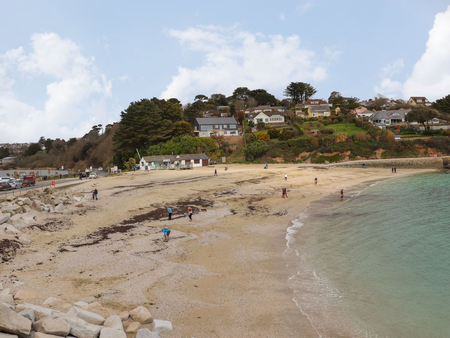 A beach with people walking near the water and houses on a hill in the background at Sea Dream in Falmouth