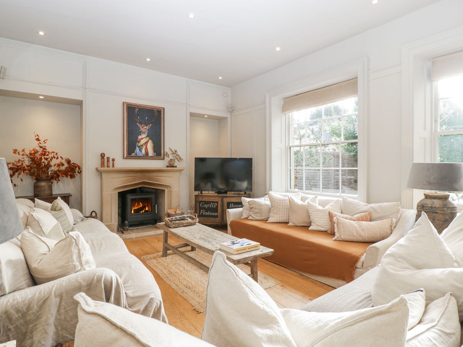 A living room with sofas pillows a wooden coffee table fireplace and a television at Cotswold House in Moreton-In-Marsh