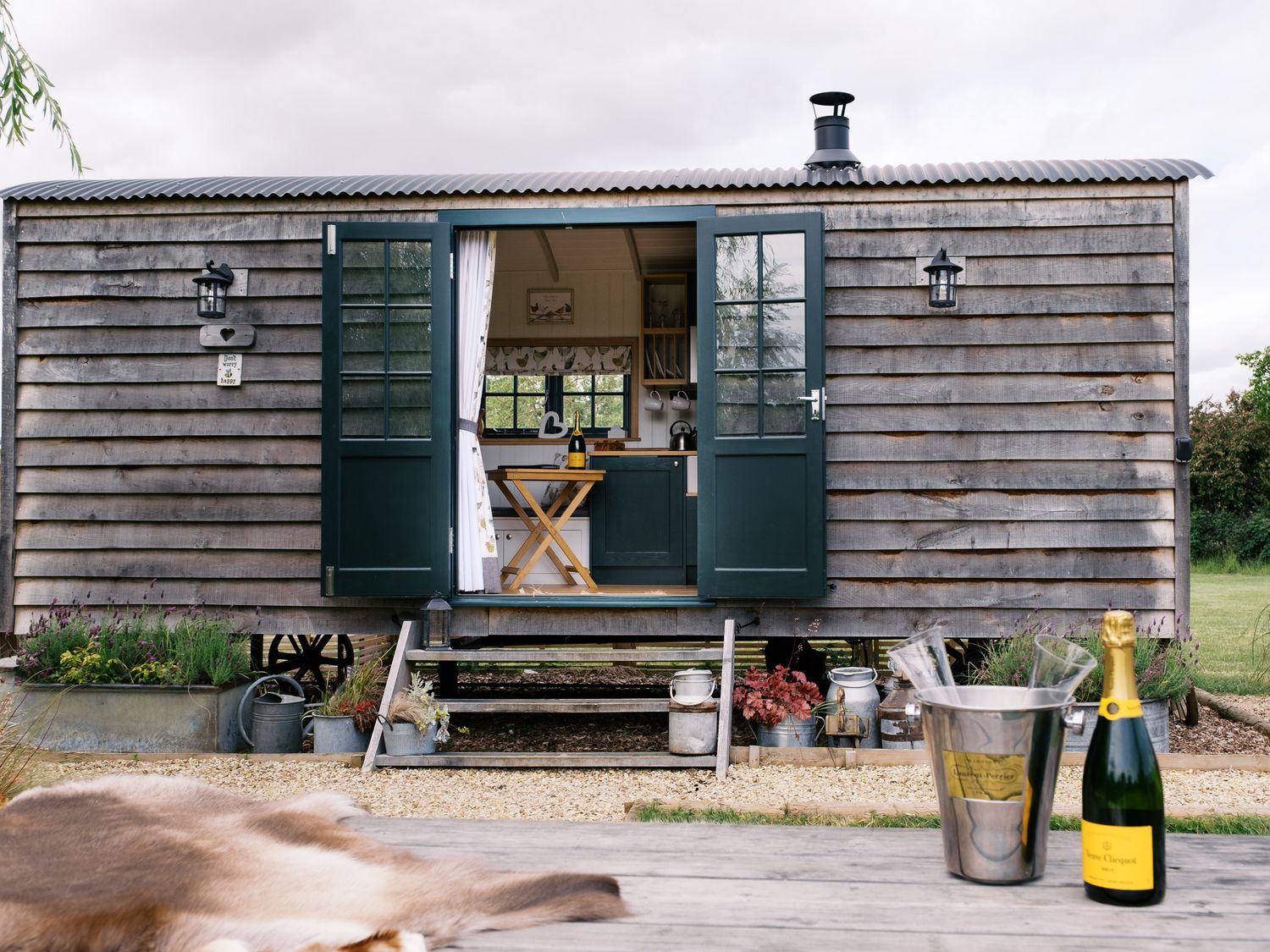 A shepherd's hut with open doors and champagne on a table at Poppie's Shepherds Hut at Shepherds Lodge Retreat and Wellness near Bottesford