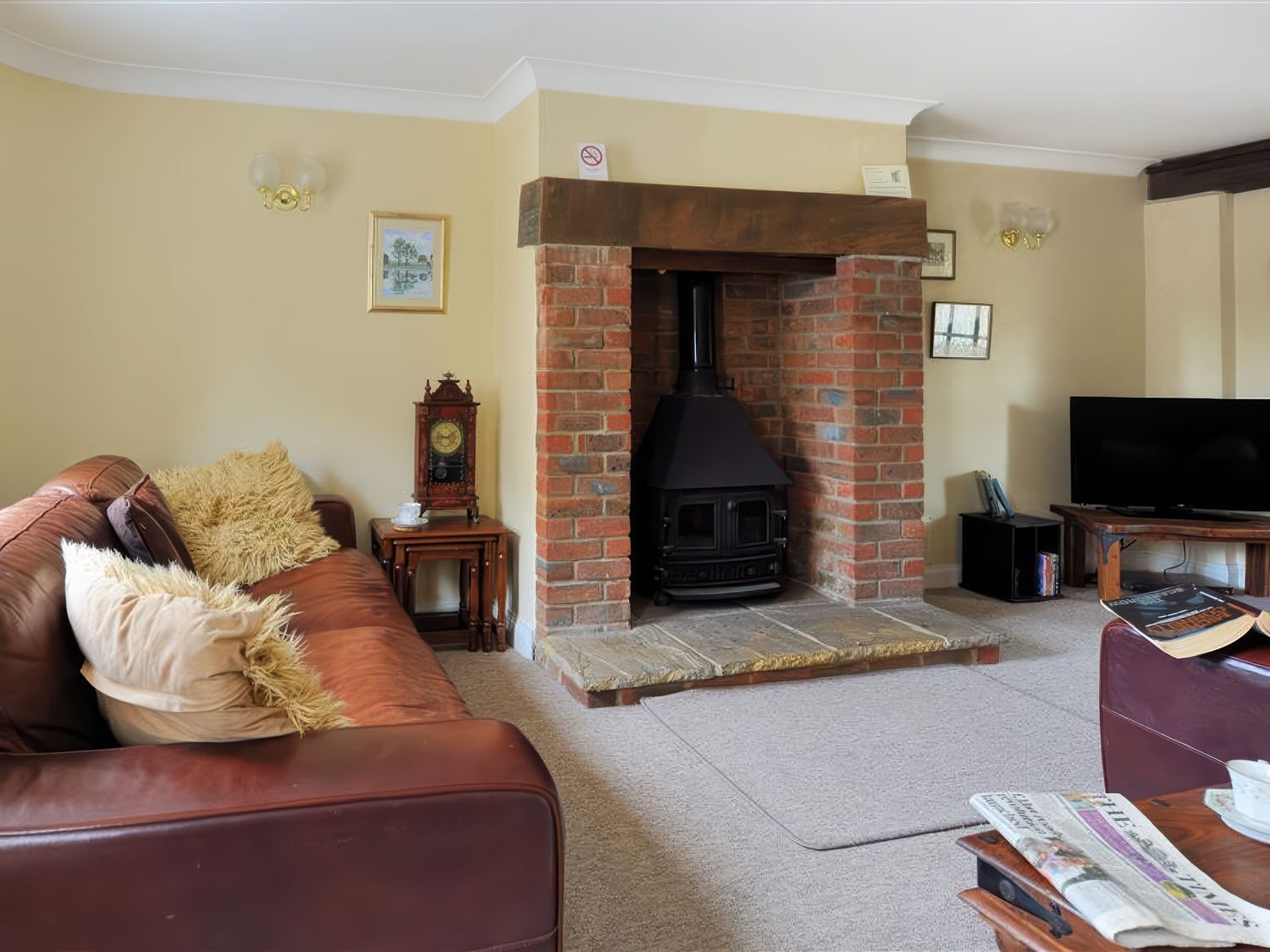 A living room with a leather sofa and a brick fireplace with a wood stove at Moonfleet Cottage in Charmouth