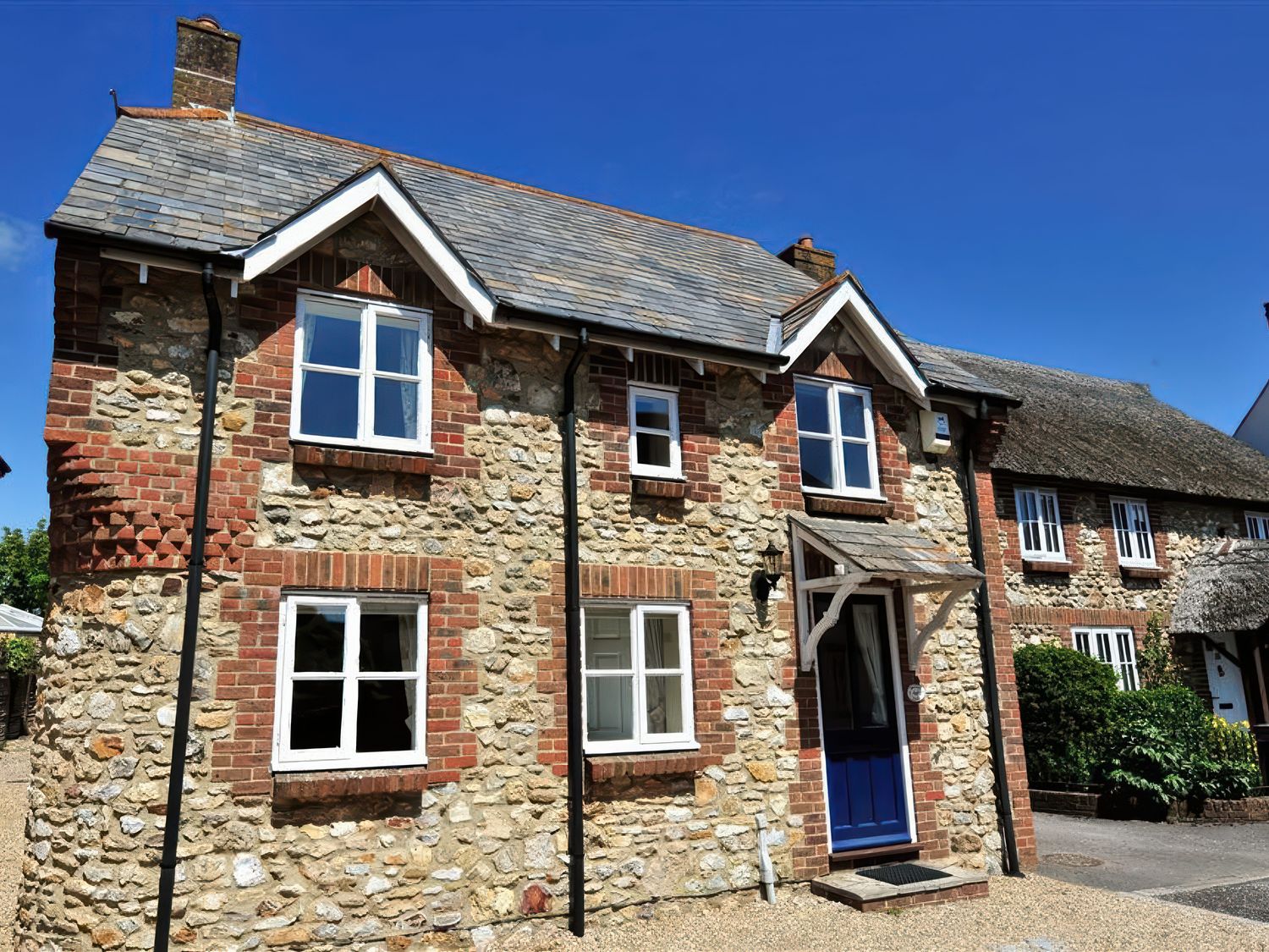 Exterior of a two-story stone and brick house with multiple windows and a blue front door at Moonfleet Cottage in Charmouth