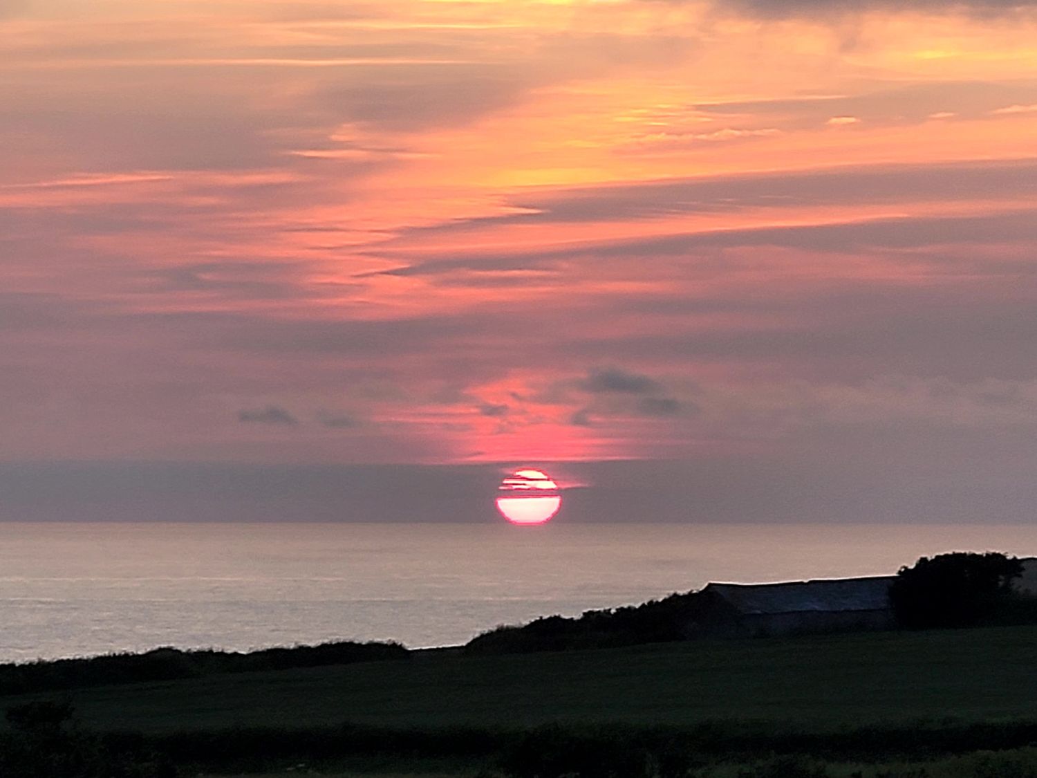 A sunset over the ocean with a silhouette of land at Badgers Sett Stibb near Kilkhampton
