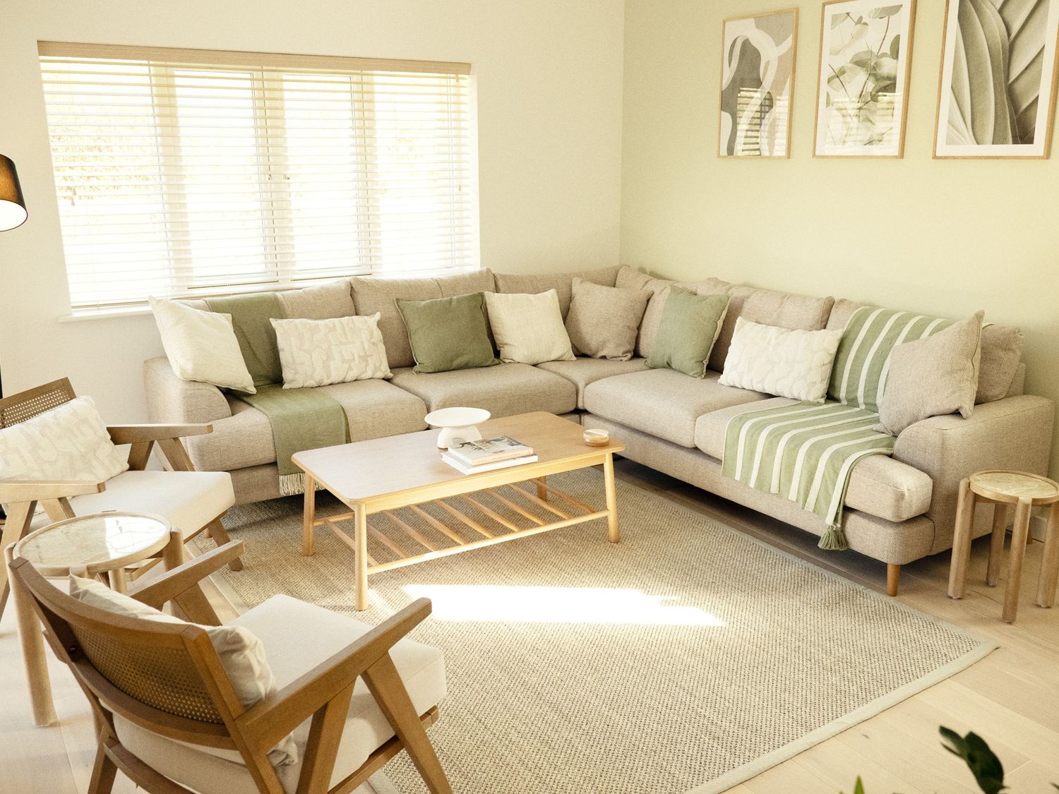 A living room with a large beige sectional sofa with pillows and throws two wooden armchairs a wooden coffee table and three framed pictures on the wall at Kerrek Lodge in Mylor Bridge