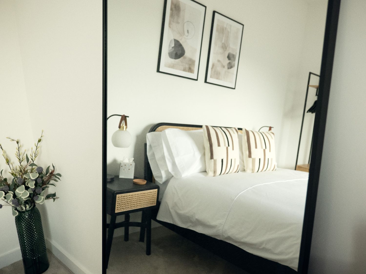 A bedroom with a bed white bedding two pillows bedside table with lamp and tissue box wall art and floor vase with flowers at Kerrek Lodge in Mylor Bridge