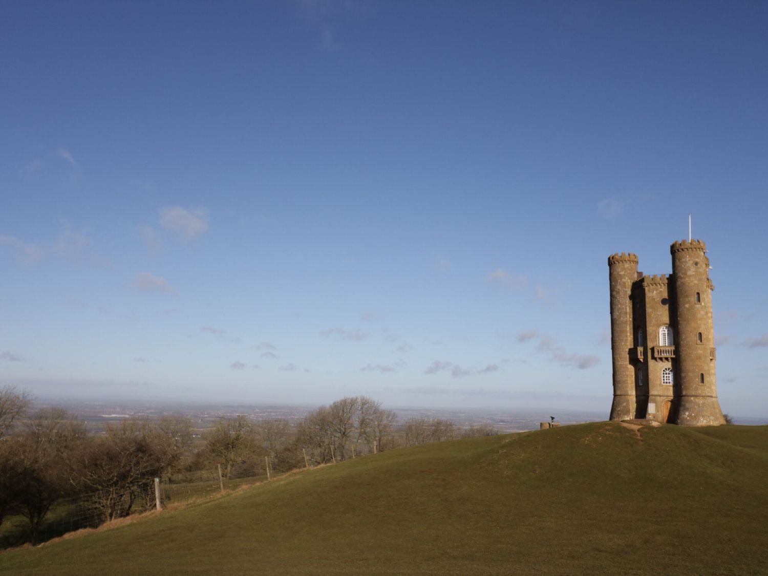 A stone tower on a grassy hill with trees and a clear sky at Tree Tops in Broadway