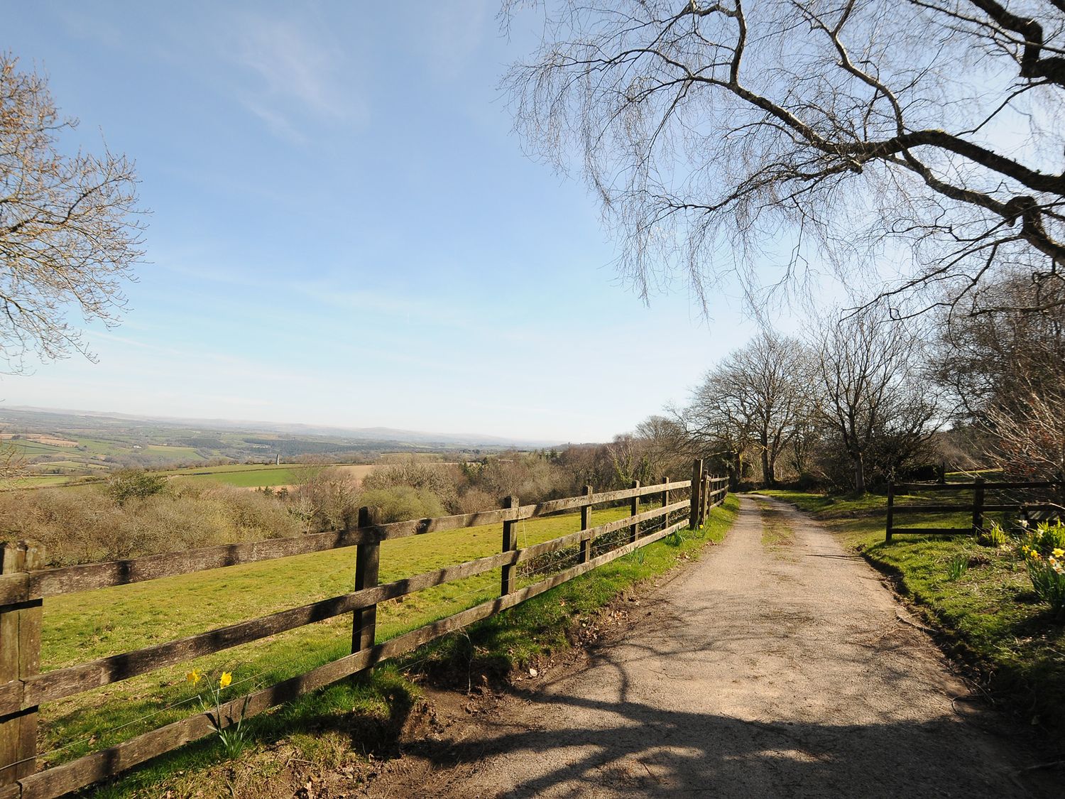A dirt road next to a wooden fence with fields and trees around Rose Cottage in Callington