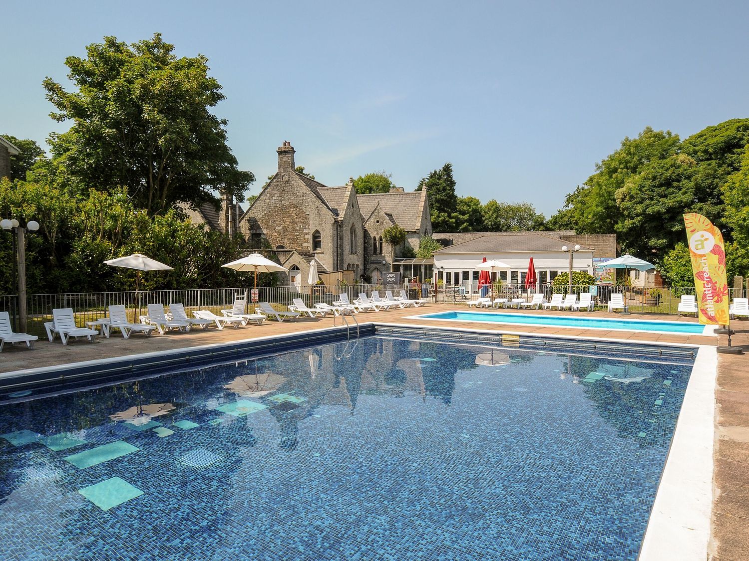 An outdoor swimming pool with lounge chairs and umbrellas near stone buildings at Satinwood White Cross near Newquay