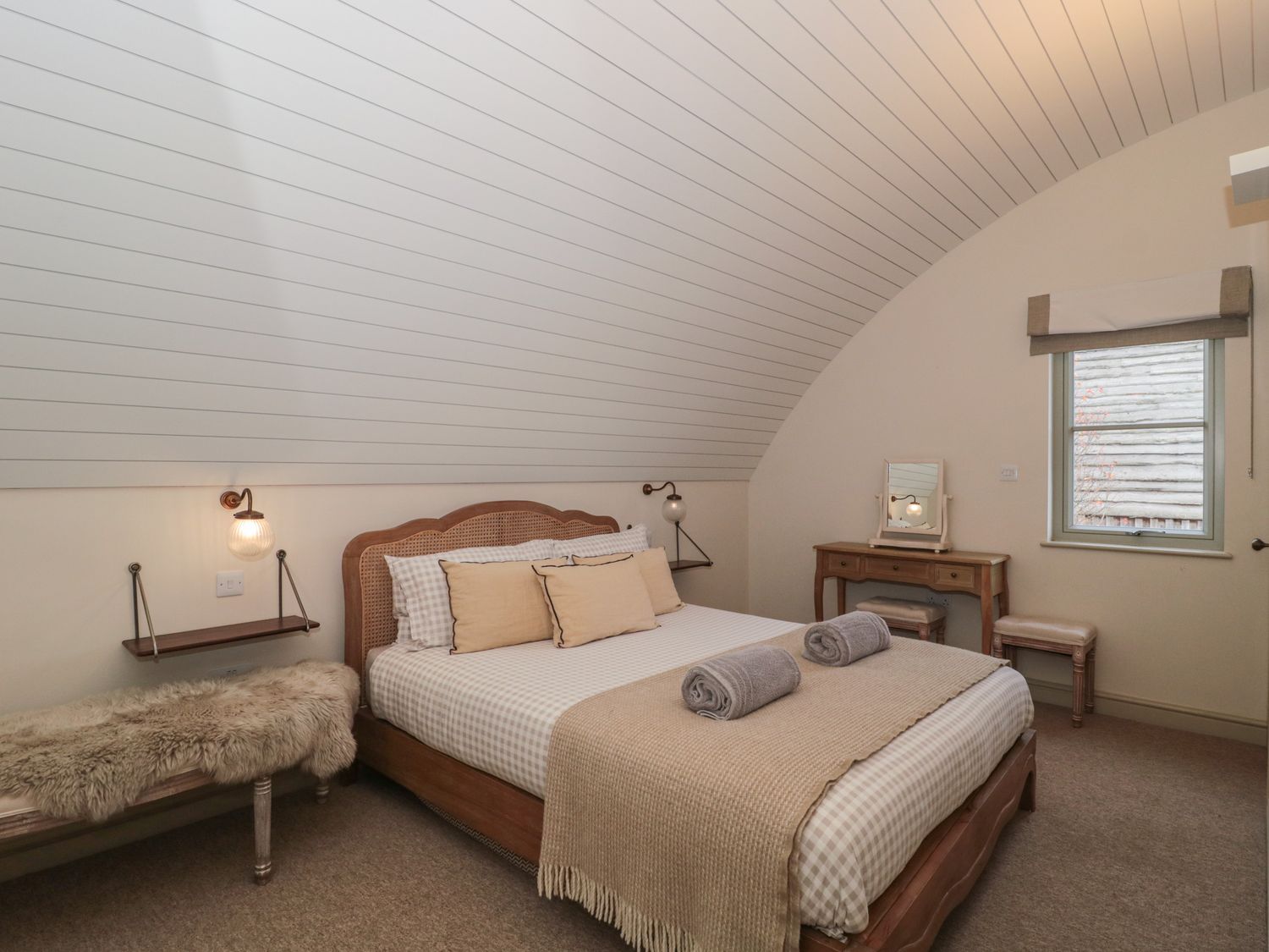 A bedroom with a double bed two rolled towels on the bed a bench with a fur throw a dressing table with a mirror and two stools at Dutch 1 Oxleaze Farm near Lechlade-On-Thames