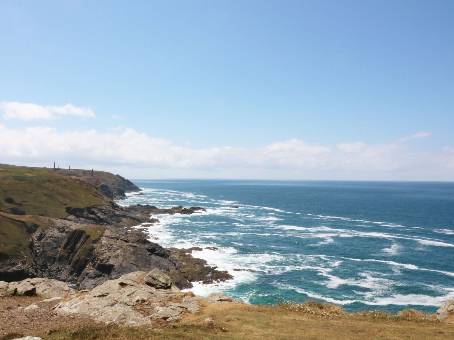 A rocky coastline with waves crashing and a clear blue sky at Little Victory in Pendeen