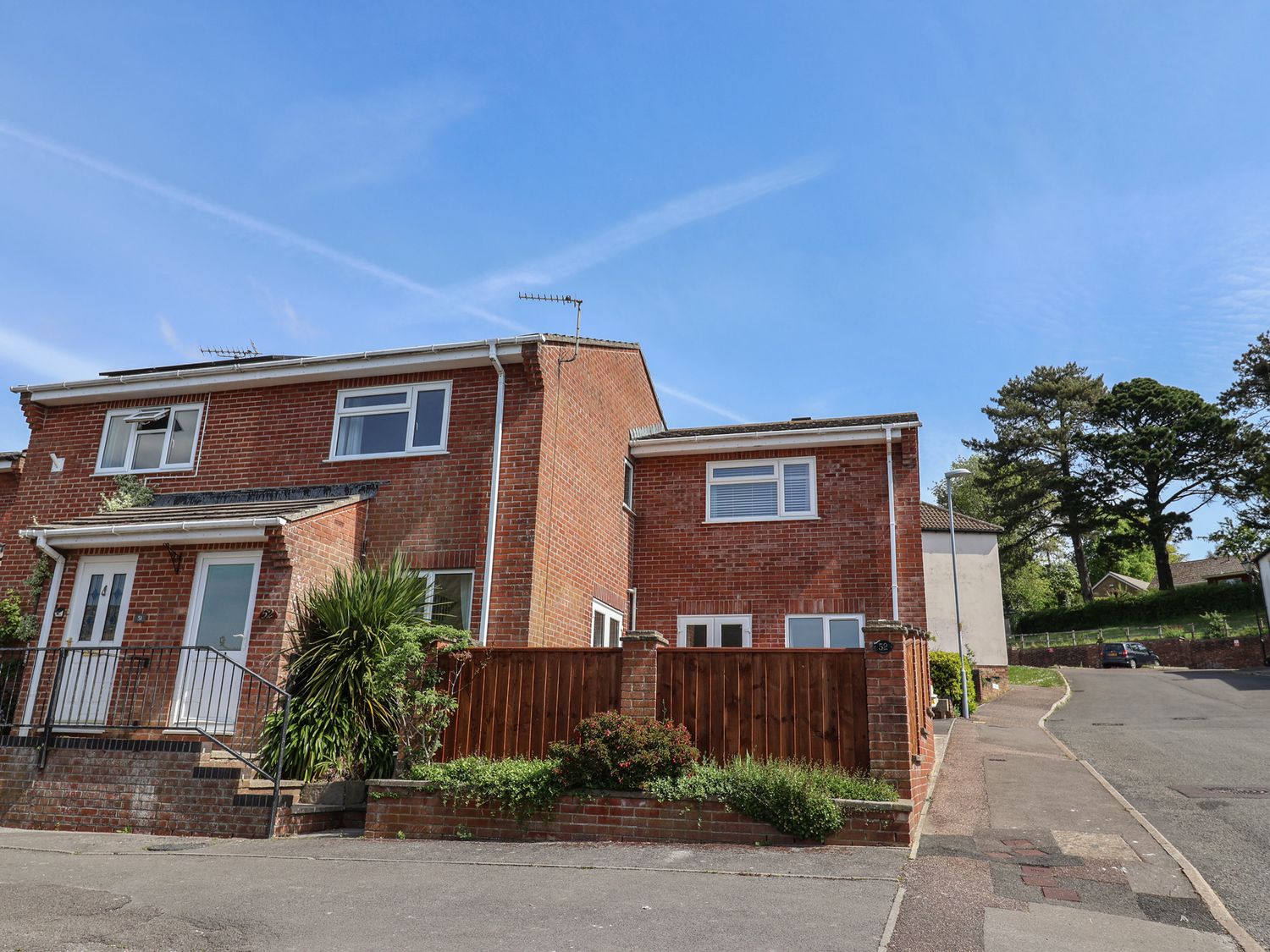 A brick semi detached house with white doors and windows on a residential street with a wooden fence and plants at SubLyme in Lyme Regis