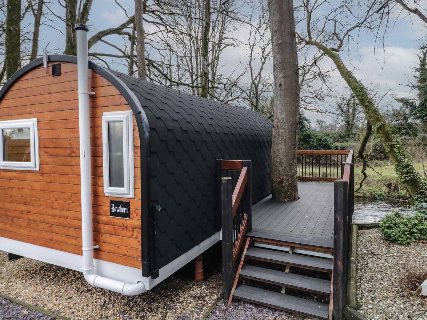 A small wooden cabin with curved black roof and deck with stairs around a tree at Hawthorn in Dungiven Londonderry