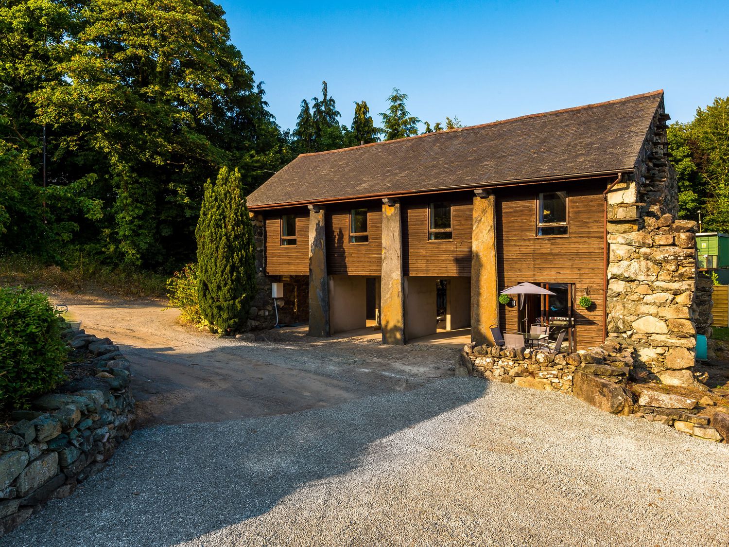 A building surrounded by trees with a gravel driveway at Idris Barn in Dolgellau
