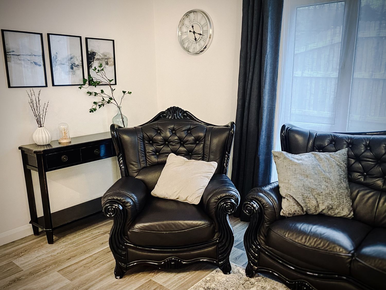 A living room with black leather armchairs and a black console table with vases near a window with dark curtains at Trelawne Near Crackington Haven
