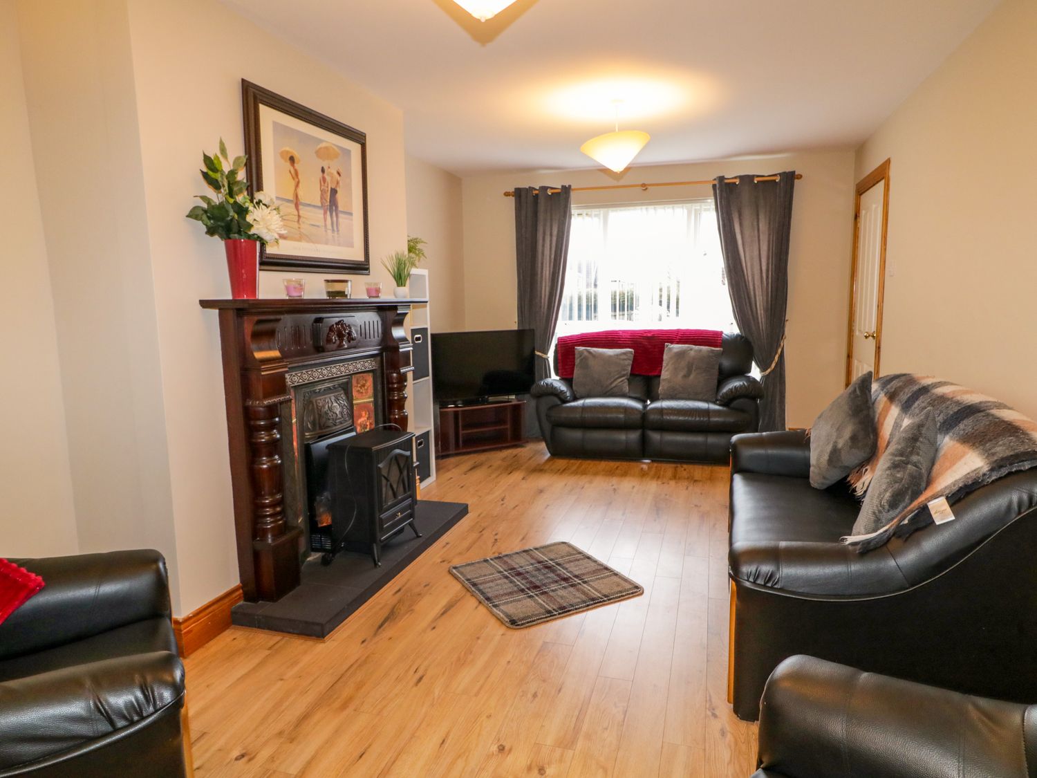 A living room with black leather sofas a wooden floor a fireplace TV and window with curtains at Portstewarts Home from Home in Portstewart County Londonderry