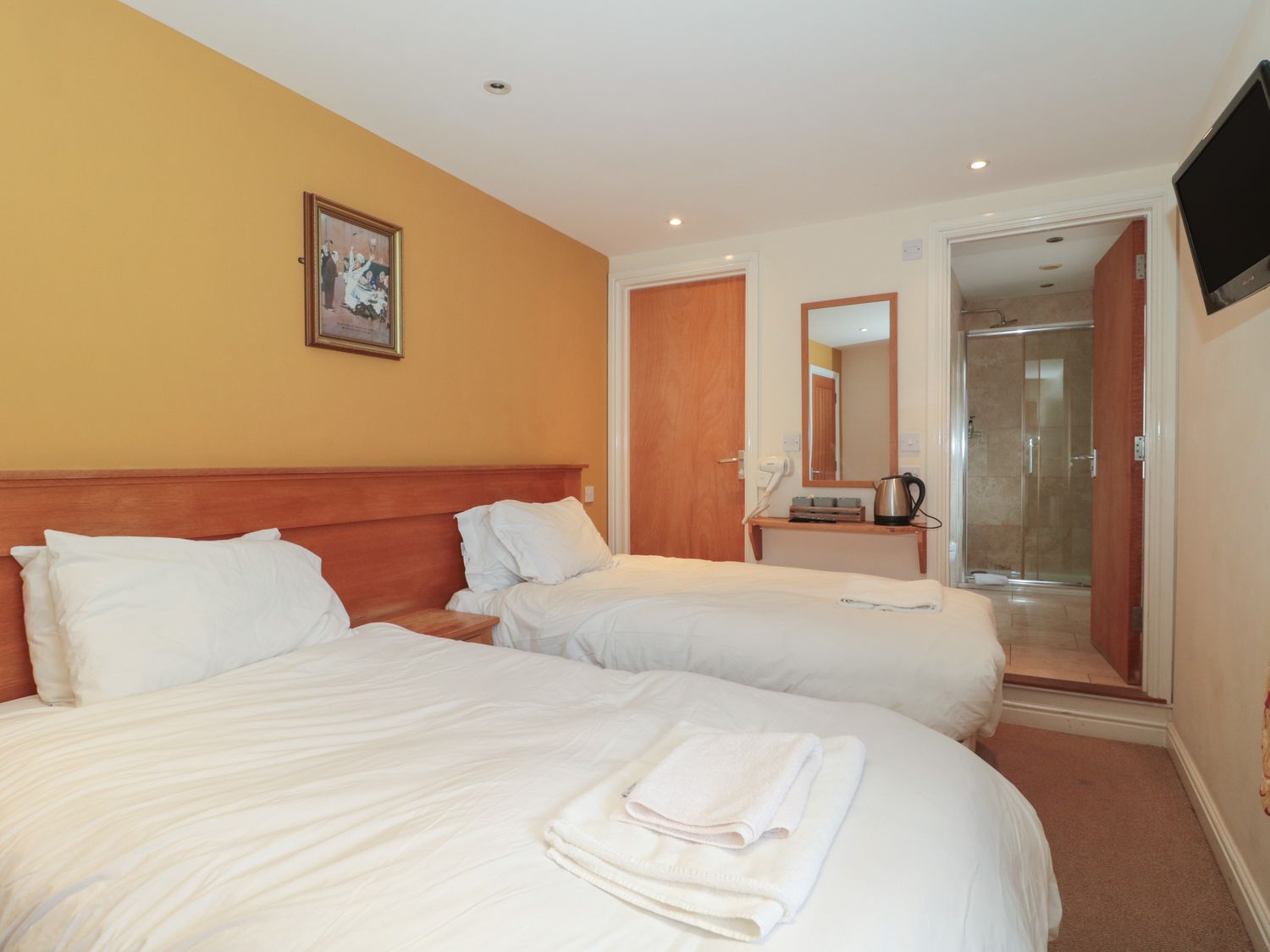 A twin bedroom with two beds a wooden headboard a bedside table a wall mirror and a door leading to a bathroom at Twin Room in Whiteshill